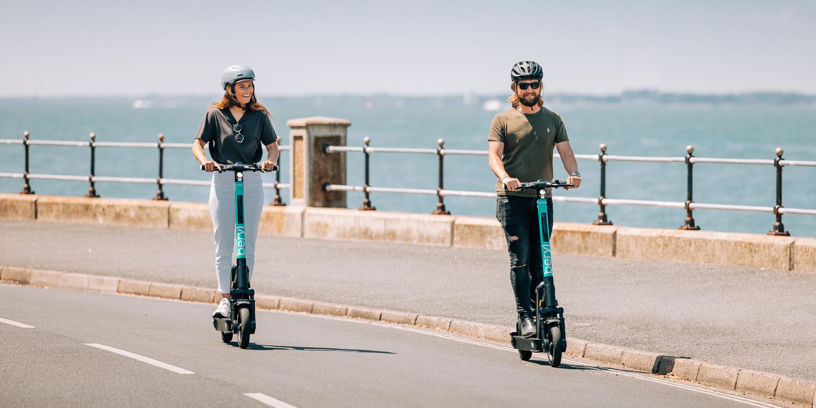 2 e-scooter riders on the road with the sea in the background 