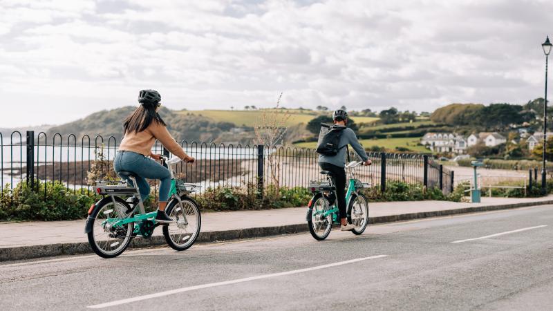 Man and woman riding Beryl bikes along coast road in Cornwall